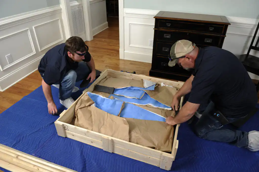 Gasperson movers carefully unloading item in crate in residential home
