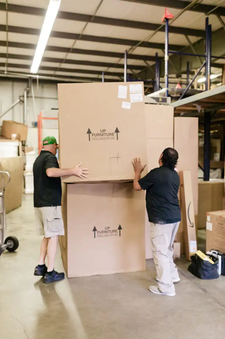 Gasperson movers stacking large moving boxes in warehouse